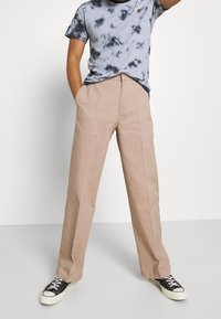 Pantalones de pierna ancha beige hechos de algodón con una textura suave, con pliegues frontales y bolsillos laterales estándar, combinados con una camiseta azul de tie-dye.