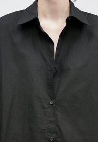 Chemise noire à boutons avec col classique, tissu texturé et patte de boutonnage avant avec des boutons noirs assortis.