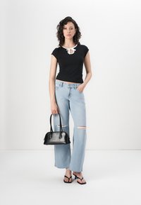 Top negro ajustado con un detalle de lazo blanco, jeans rasgados azul claro, bolso negro y chanclas negras. Atuendo simple y casual.