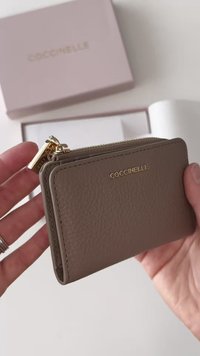 Brązowy skórzany portfel o teksturowanym wykończeniu i złotym suwakiem, z wytłoczonym na przodzie logo marki "Coccinelle".