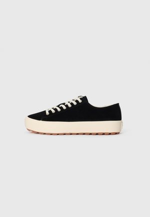 Svart semsket sneaker med kremfarget gummisåle, rund tå og kremfargede snørebånd. Har en teksturert såle med spor for bedre grep.