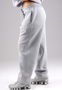 Person wearing gray sweatpants with drawstring and silver athletic shoes with spring-like soles on plain background.