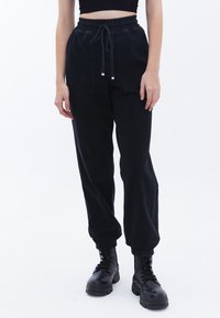 Pantalones jogger de mezclilla negra con cintura elástica y cordón, con puños elásticos y dos bolsillos frontales. Textura suave.