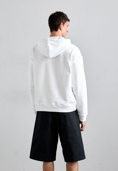 Hoodie alb cu buzunar tip cangur și glugă cu șnur, asociat cu pantaloni scurți negri. Material fin, croială lejeră și mâneci scurte.