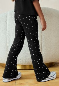 Mustad lõhikutega püksid valgete tähtmustritega, puuvillane kangas, elastse vöökohaga ja valgete tossudega.