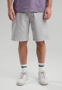 Light gray cotton shorts with a straight cut, elastic waistband, and side pockets, paired with white sneakers and striped socks.