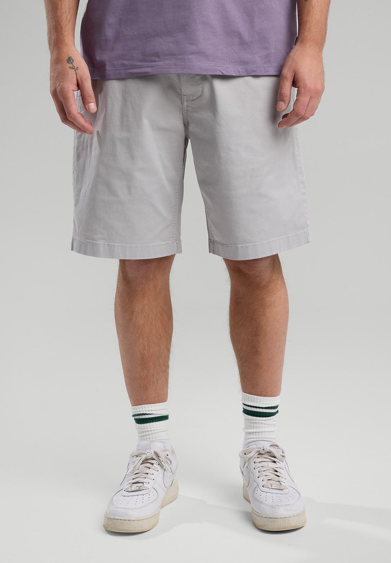 Light gray cotton shorts with a straight cut, elastic waistband, and side pockets, paired with white sneakers and striped socks.