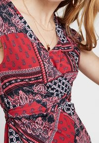 Rotes und schwarzes gemustertes Kleid mit V-Ausschnitt, Wickeldesign und schmalem Gürtelakzent. Es zeichnet sich durch komplizierte Paisleymuster und florale Motive aus.