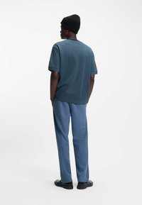 Tiilin sävyinen ribbineuloksinen lyhythihainen paita yhdistetty vaaleansinisiin kapeneviin housuihin. Housuissa on vetoketjut lahkeensuissa ja ne on yhdistetty mustiin kenkiin.