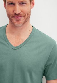 V-hals t-shirt van zacht groen stof, met een gladde textuur en korte mouwen. Strak aansluitend ontwerp met subtiele stikseldetails.
