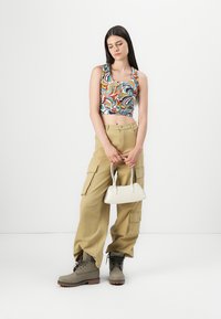 Un débardeur coloré avec un motif abstrait, un pantalon cargo beige, des bottes grises et un petit sac à main blanc pour une tenue décontractée.