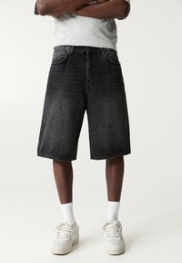 Shorts in denim grigio scuro con una vestibilità ampia, caratterizzati da un classico design a cinque tasche e una vita media. Abbinati a sneakers bianche e calze.