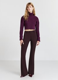 Häkel-Turtleneck-Pullover in Dunkelpurpur, kombiniert mit hoch taillierten, dunkelbraunen, ausgestellten Hosen. Glatte Textur, figurbetonte Silhouette und klare Linien.