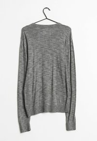 Grå långärmad tröja med rund hals, tillverkad av ett texturerat stickat material, med ribbade manschetter och fåll, upphängd på en svart galge.