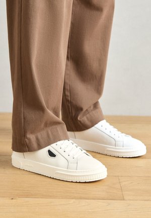 Hvite lær sneakers med lav profil, rund tå og svart detalj på sidene. Snørene og den teksturerte gummisålen er synlige.