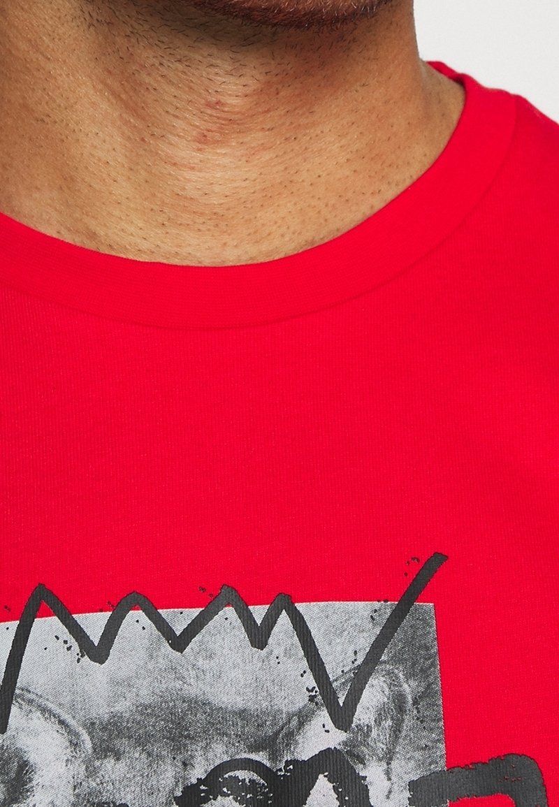 T-shirt en coton rouge avec un col rond, arborant un imprimé graphique en noir et gris, comprenant des lignes dentelées et un élément photo.