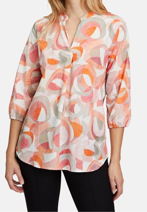Blouse multicolore avec un motif géométrique dans des teintes douces d'orange, de rose et de gris. Disponible avec une coupe légèrement décontractée et des manches trois-quarts.