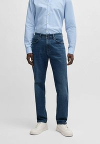 Mörka jeans med rak passform, femficksdesign och subtila sömdetaljer, tillsammans med en ljusblå skjorta med knappar.