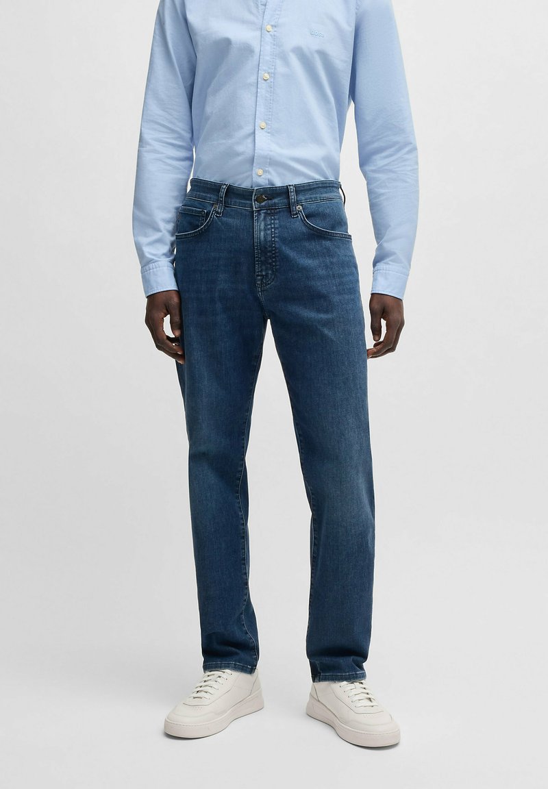 Mörka jeans med rak passform, femficksdesign och subtila sömdetaljer, tillsammans med en ljusblå skjorta med knappar.