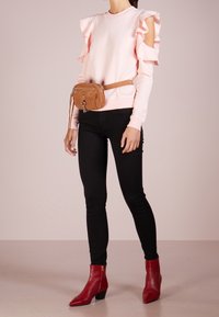 Sudadera rosa claro con mangas con volantes, vaqueros pitillo negros y botines rojos hasta el tobillo. Riñonera marrón llevada en la cintura, con cremallera.