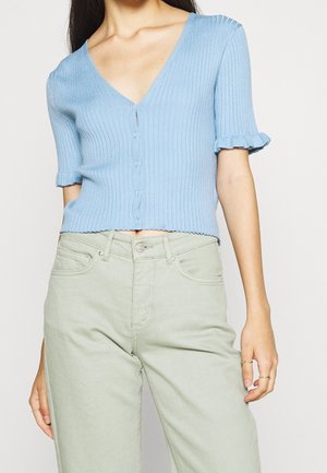 Haut en maille côtelée bleu clair avec un décolleté en V profond, des manches courtes à volants et une fermeture à boutons ; associé à un pantalon taille haute vert clair.