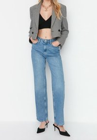 Blazer recortado a cuadros en blanco y negro, camiseta corta negra, jeans de cintura alta en azul claro y tacones negros de punta. Texturas suaves.