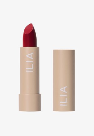 Il rossetto ILIA in un tubo beige con branding bianco; presenta una bullet rossa vibrante e liscia con una punta sagomata per un'applicazione precisa.