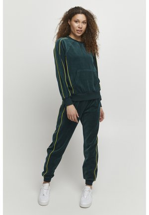 Completo in velluto di colore verde scuro con strisce laterali gialle. Presenta una tasca frontale sulla parte superiore e polsini elasticizzati sia sulla parte superiore che sui pantaloni.