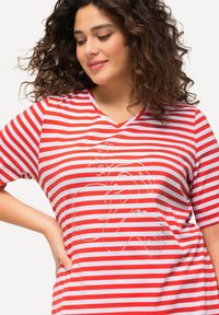Camiseta de manga corta con cuello en V a rayas rojas y blancas, con un dibujo lineal simple de un flamenco y corazones en el frente. Textura de tela suave.