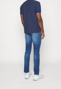 Námořnické polo tričko s modrým lemem, kombinované s přiléhavými modrými džínami a bílými teniskami. Důraz na materiály a barevné kontrasty.