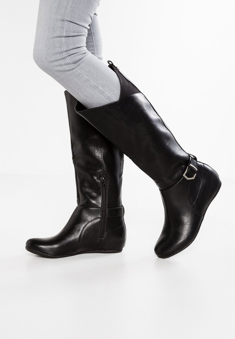 Bottes noires jusqu'au genou en cuir synthétique lisse, avec une fermeture éclair sur le côté, un accent de sangle et un bout rond. Semelle en caoutchouc avec un talon bas.