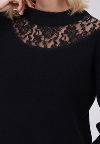 Czarny sweter z teksturowanym dzianinowym korpusem i koronkowym wykończeniem przy dekolcie, tworzącym kwiatowy wzór na skórze.