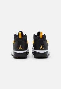 Černé a žluté sportovní boty mají strukturovaný svršek vyrobený z prodyšné a syntetické materiály, výrazné bílé podešve a akcent s logem na patě.