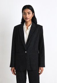 Sacou elegant cu dungi negre, realizat dintr-un material texturat, având închidere cu un singur buton și rever cu tăietură în formă de U. Dungile orizontale și verticale adaugă detaliu.