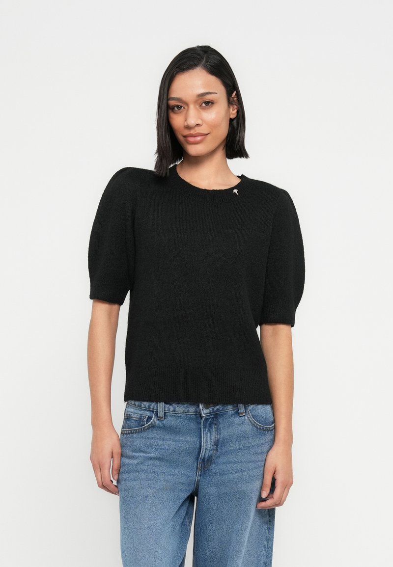 Pulover negru tricotat cu mâneci scurte bufante și decolteu rotund. Are un mic accent lângă gât. Poartă-l cu blugi bleu deschis.