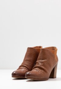 Bottines en cuir tressé marron avec un bout lisse, une tige texturée et un talon empilé. Elles présentent une fermeture éclair sur le côté pour un enfilage facile.