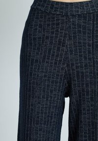 Närbild av mörkblå texturerade tygbyxor med ett rutmönster, som visar midjebandet och övre benområdet.