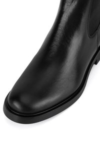 Must mustaed jalatsid, millel on peen disain, ümar varvas ja lame kummitald. Omaduseks on sile tekstuur ja elastsed külgpaneelid.