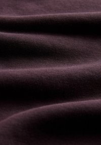 Ciemnofioletowa bawełniana tkanina o gładkiej fakturze, z delikatnymi żeberkami i fałdami, podkreślająca jej zwis i miękkość.