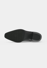 Semelle de chaussure en cuir noir avec grip texturé à l'avant et talon lisse et côtelé, présentée sur un fond clair uni.