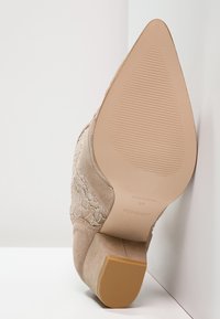 Beige semišové kotníkové boty se špičatou špičkou, vyšívanými detaily a nízkým blokovým podpatkem, podrážka s označením značky a velikosti.
