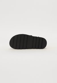 La suela del zapato negro presenta una superficie texturizada con surcos horizontales para mayor tracción, puntera redondeada y un diseño plano y ancho.