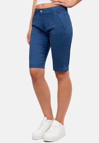 Pantaloni corti blu fino al ginocchio realizzati in un tessuto liscio con tasche anteriori. Presentano una chiusura con bottone e dettagli cuciti lungo la vita e i lati.