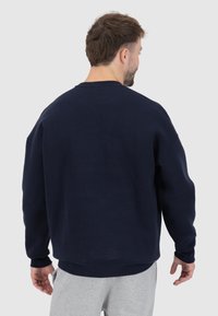 Felpa blu navy con collo rotondo, spalle cadenti e polsini a costine. Materiale morbido, vestibilità leggermente rilassata, cuciture resistenti.