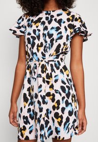 Robe à imprimé léopard en rose clair, avec des taches noires, bleues et jaunes, manches courtes à volants et ceinture à nouer à la taille.