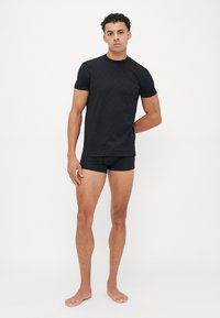 T-shirt nera aderente con strisce testurizzate, abbinata a pantaloni corti neri. Tessuto liscio, maniche corte e design minimalista.