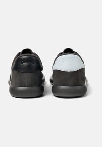 Black and grey sneakers made of suede and leather, featuring a smooth texture, rounded shape, and minimalist design with logo accents.