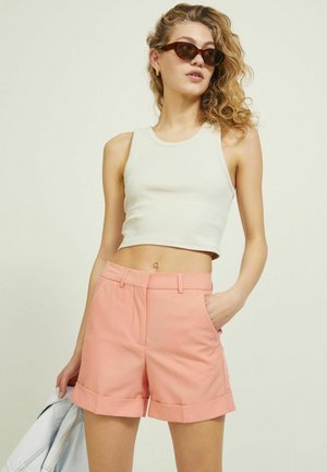 Svijetlosivi rebrasti crop top i ružičaste hlače visokog struka s preklopljenim manžetama, koje imaju bočne džepove i glatku teksturu. Model s komentarima.