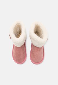 Bottes en daim rose avec un revers et une doublure blancs duveteux, dotées d'un bout arrondi et de coutures visibles le long de la semelle.