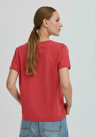 T-shirt en coton rouge à manches courtes, coupe décontractée et col rond, associée à un jean en denim bleu clair avec une couture décorative.